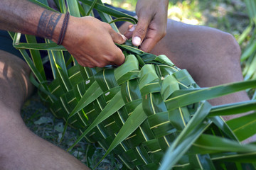 Fijian man preparing a basket mad out of palm tree leaves full with meat for Lovo