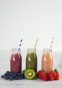 Three Different Fruit Smoothy on a White Wood Table - Berry, Green, and Strawberry Banana