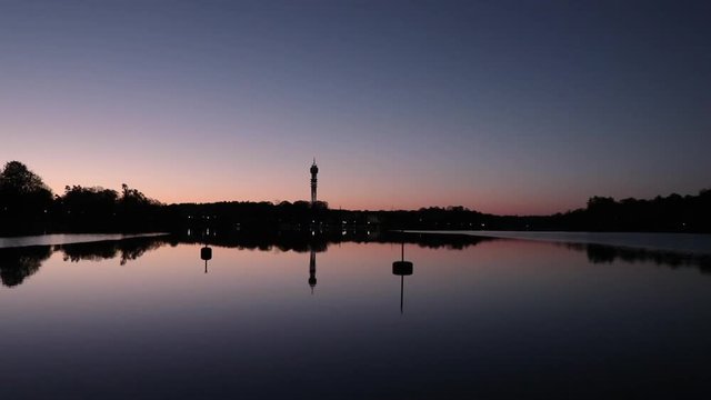 Morning at Djurg&aring;rden in Stockholm, Sweden. The tower Kakn&auml;stornet and a line of trees is reflected in the still water. The sky is clear above it.