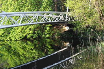A reflection of a white bridge in water among green bushes and trees