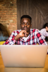 Handsome Afro American man in casual clothes holding a cup of coffee and using laptop.