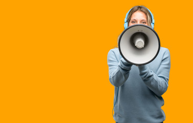 Young beautiful woman listening to music communicates shouting loud holding a megaphone, expressing success and positive concept, idea for marketing or sales