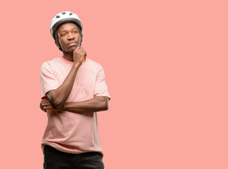Black man wearing bike helmet thinking and looking up expressing doubt and wonder