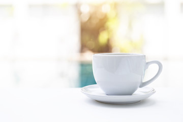 White ceramic coffee cup over blurred swimming pool background, morning outdoor day light