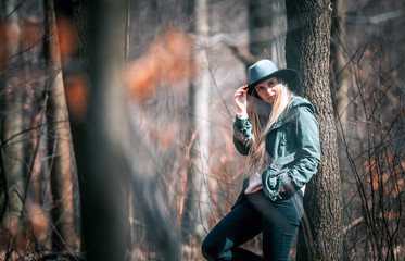 Naklejka premium Portrait of beautiful woman with long blond hair in hat walking in forest at sunny day