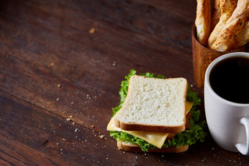 Breakfast table with sandwich and black coffee on rustic wooden background, close-up, selective focus