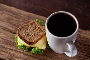 Breakfast table with sandwich and black coffee on rustic wooden background, close-up, selective focus