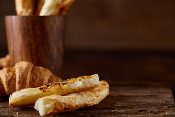 Puff pastries on piece of board over dark wooden table, close-up, selective focus, backlight.