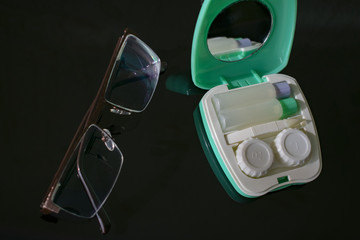 container for contact lenses with tweezers and a mirror with glasses lying next to them on the table