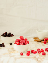 Raw raspberries and wild black, blackberries in white cups. Light marble background. Summer fruit, berries. Detox diets and healthy food concept.