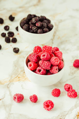 Raw raspberries and wild black, blackberries in white cups. Light marble background. Summer fruit, berries. Detox diets and healthy food concept.