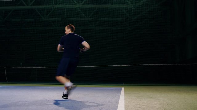 Serve by professional tennis player. Tennis serve indoor of tenis hall. Man on serve with tenis racket and dressed in black t-shirt, black shorts and black shoes.