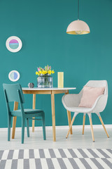 Chair, armchair with a pillow, dining table, striped carpet and plates on a green wall in a colorful dining room interior