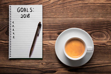 2018 GOALS on his notebook. New year resolutions concept. Top view.