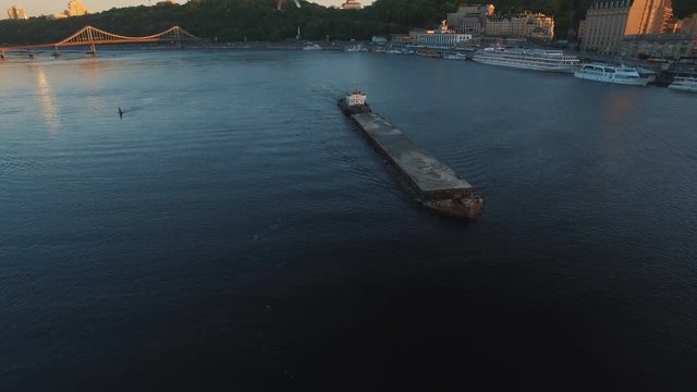 Barge sails along the river near the city port on sunset aerial footage