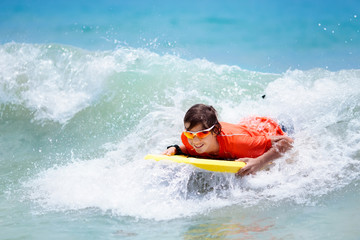 Fototapeta na wymiar Child surfing on tropical beach. Surfer in ocean.