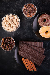 Top view of chocolate tablets, donuts, brown sugar with peanuts in chocolate and coffee beans on dark vintage wooden background