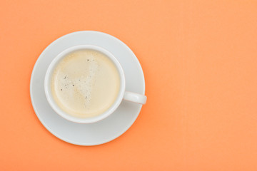 White porcelain cup of black coffee on saucer on peach color background