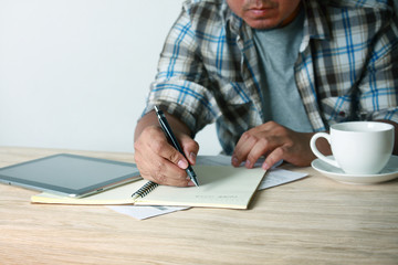 A man wearing a plaid shirt writing on a desk