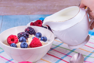 A cup of oatmeal with fresh berries and a jug of milk - a concept of dietary nutrition