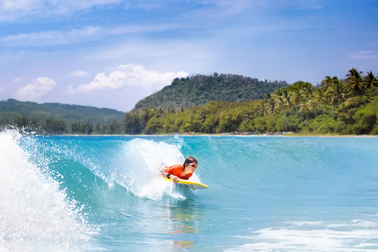 Child surfing on tropical beach. Surfer in ocean.