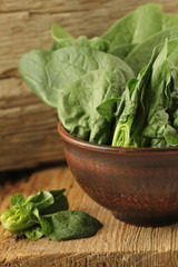 Fresh green leaves of spinach in a bowl on old wooden background.