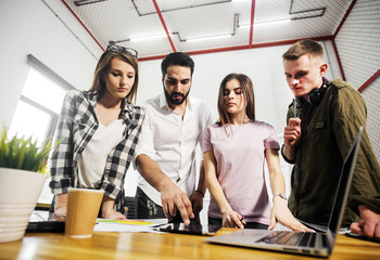 Team of office workers discussing information on laptop on working place table, indoor shot in...