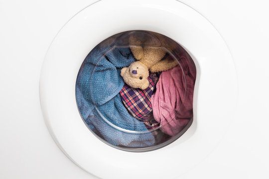 Wild Carousel Ride / Window door of washing machine with laundry and toy teddy bear inside who takes a look out (copy space)