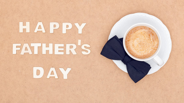 Happy Father's Day Background. Cup of coffee and black bow tie on brown background flat lay. Fathers day still life.