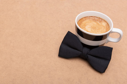 Happy Father's Day Background. Cup of coffee and black bow tie on brown background flat lay. Fathers day still life.