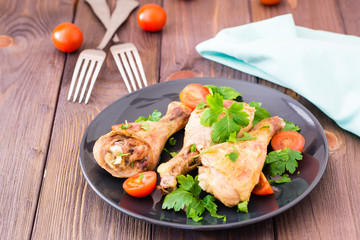 Baked chicken legs in spices with tomatoes and greens in a plate on a wooden table