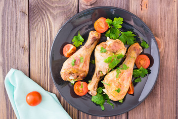 Baked chicken legs in spices with tomatoes and greens in a plate on a wooden table. Top view