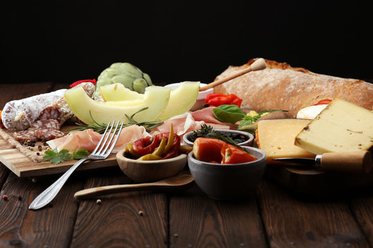 Italian antipasti wine snacks set. Cheese variety, Mediterranean olives, pickles, Prosciutto di Parma with melon, salami.