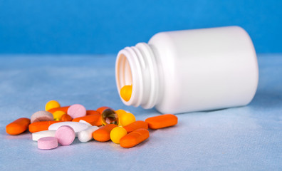 colored pills poured from a plastic jar on a blue background.