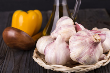 garlic in a basket with yellow pepper and a wooden spoon on  wooden table