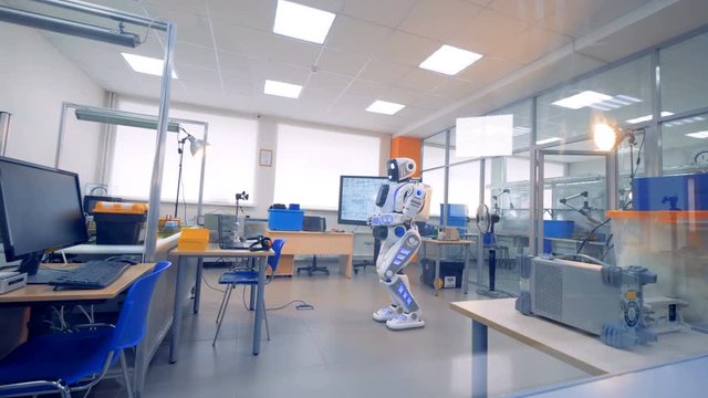 A cyborg is standing still in the middle of an engineering laboratory