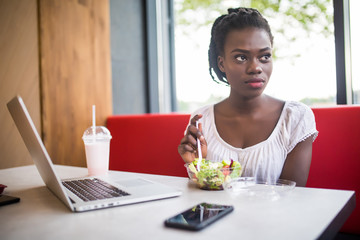 Beautiful woman have lanch eat salad at dinner sitting at cafe. Young african american woman sitting in a coffee shop and working on laptop.