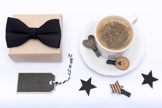 Happy Father's Day Background. Cup of coffee, beautiful present and black bow tie on white background flat lay. Fathers day still life setup.