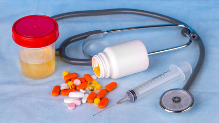 Urine container,  syringe, phonedoscope and colored pills on blue background.
