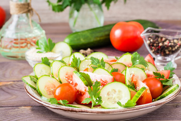 Vegetable salad of fresh cucumbers, tomatoes, parsley and sesame seeds on a plate on a wooden table