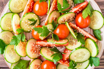 Vegetable salad of fresh cucumbers, tomatoes, parsley and sesame seeds on a plate. Top view