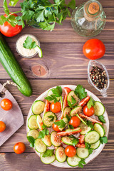 Vegetable salad of fresh cucumbers, tomatoes, parsley and sesame seeds on a plate on a wooden table. Ingredients for salad preparation. Top view