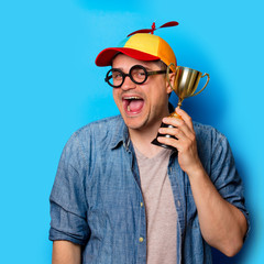 Young nerd man with noob hat holding an golden cup on blue background