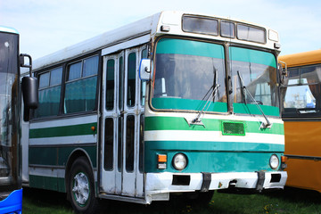 An old striped green city bus with round headlights and sliding doors parked among other buses.