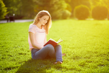 Naklejka na ściany i meble Girl reading book sitting on grass