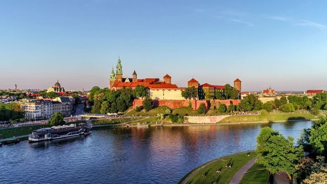 Krakow, Poland. Wawel royal Castle and Cathedral, Vistula River, park, promenade and walking people. Cracow old city with historic churches in the background. Aerial 4K flyby video at sunset in spring