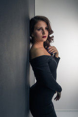 Fototapeta premium Beautiful girl in a sexy black dress posing while standing against a wall