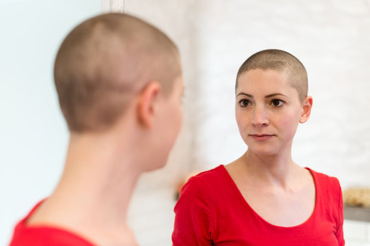 Young adult female cancer patient looking in the mirror.