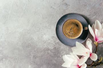 Blue cup of black espresso coffee and spring flowers magnolia branches over grey texture...