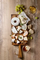 Fotobehang Cheese plate assortment of french cheese served with honey, walnuts, bread and grapes on rustic wooden serving board with glass of white wine over wood texture background. Top view, space. © Natasha Breen